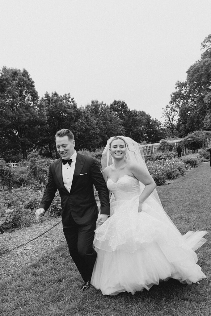 black and white photo of bride and groom running through gardens
