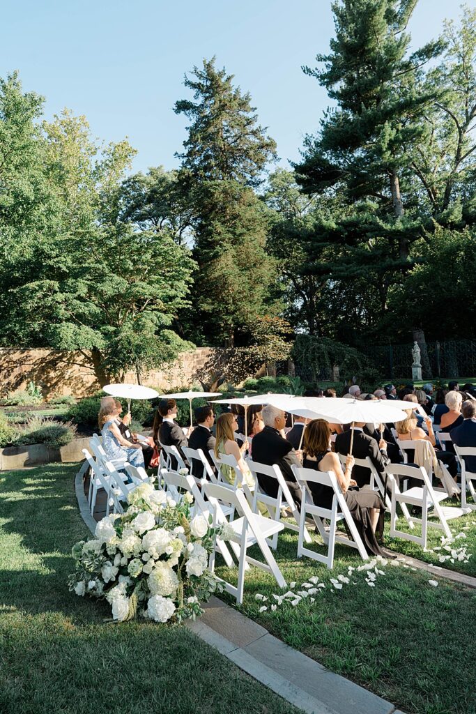 wedding guests wait at ceremony with parasol's for bride's arrival