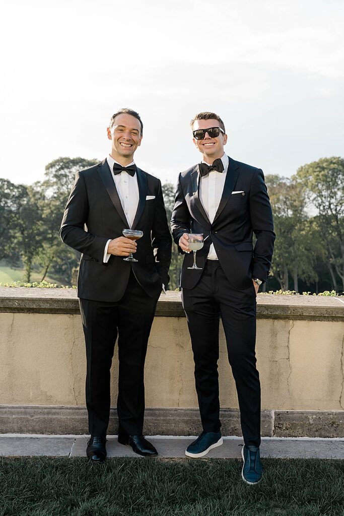 two men with drinks in black tuxes at cocktail hour